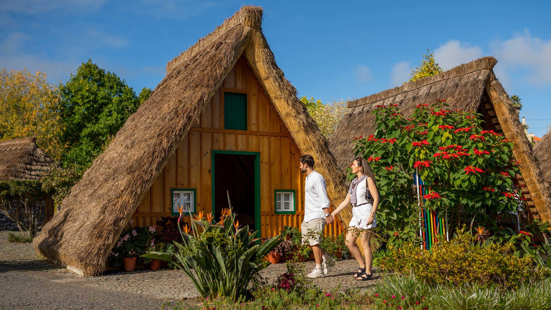Pareja entre flores y plantas junto a casas triangulares en Madeira.