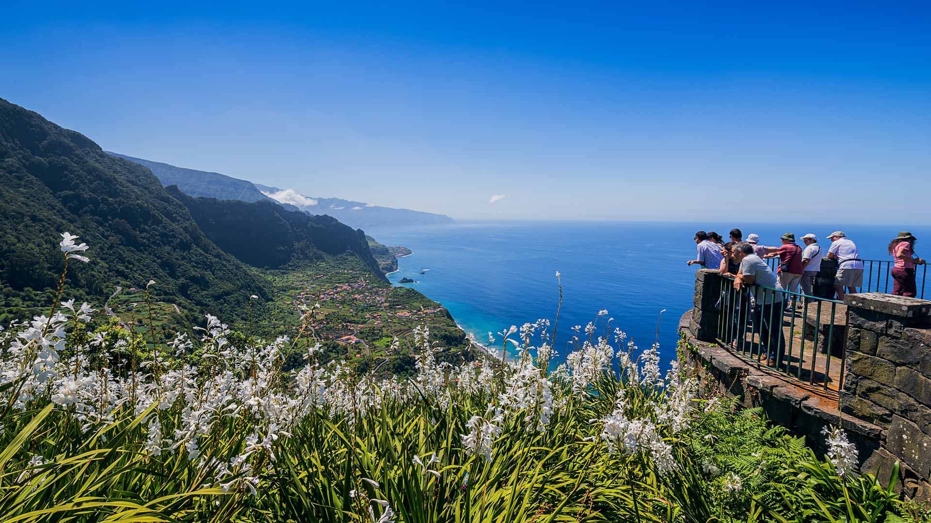 Menschen auf einem Aussichtspunkt mit Blick auf Meer und Berge.