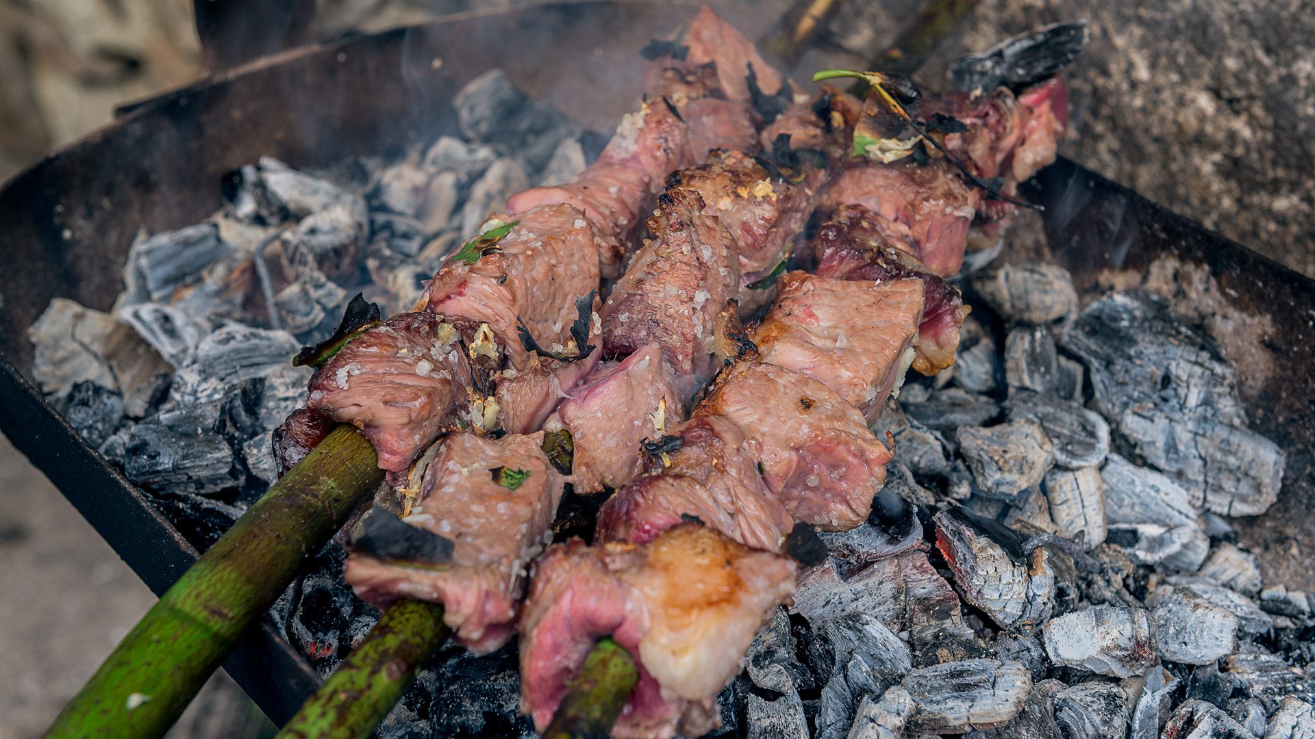 Tres pinchos de laurel con espetada cocinándose sobre un brasero.