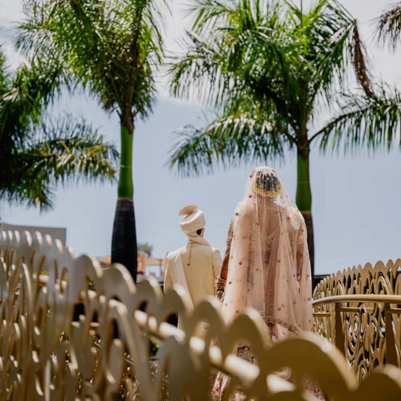 Couple in wedding attire on a bridge surrounded by palm trees.
